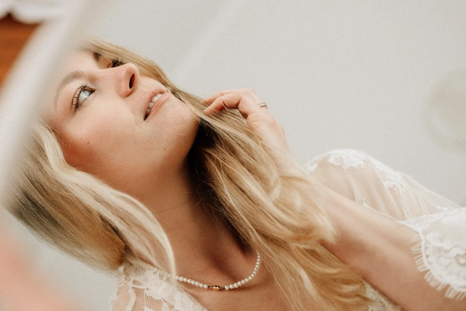 Frau in weißer Spitze mit Perlenkette schaut lächelnd nach oben, helles Boudoir im Studio Jork