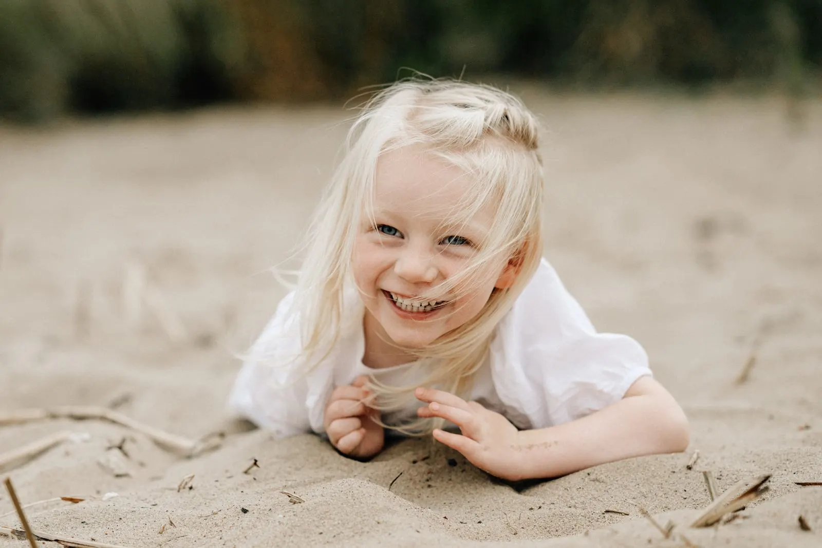 Lachendes Mädchen liegt im Sand am Elbstrand, Haare im Wind