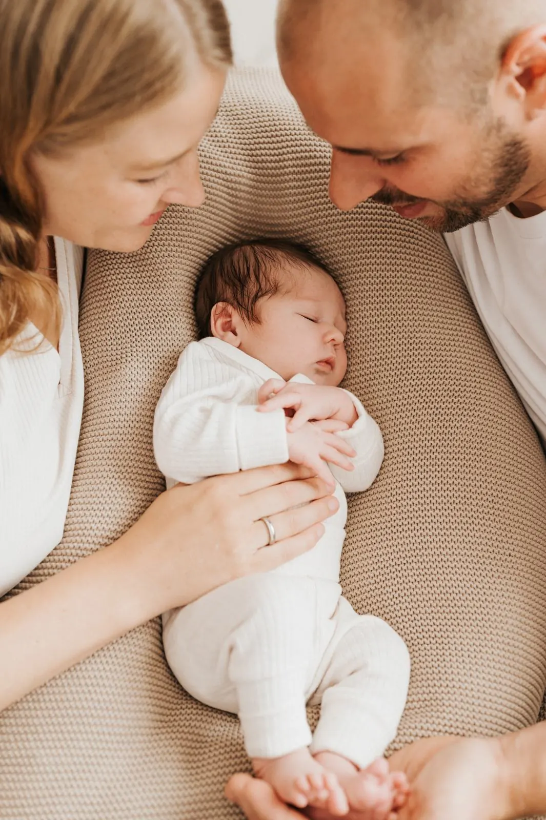 Eltern beugen sich über ihr schlafendes Baby auf einem Strickkissen