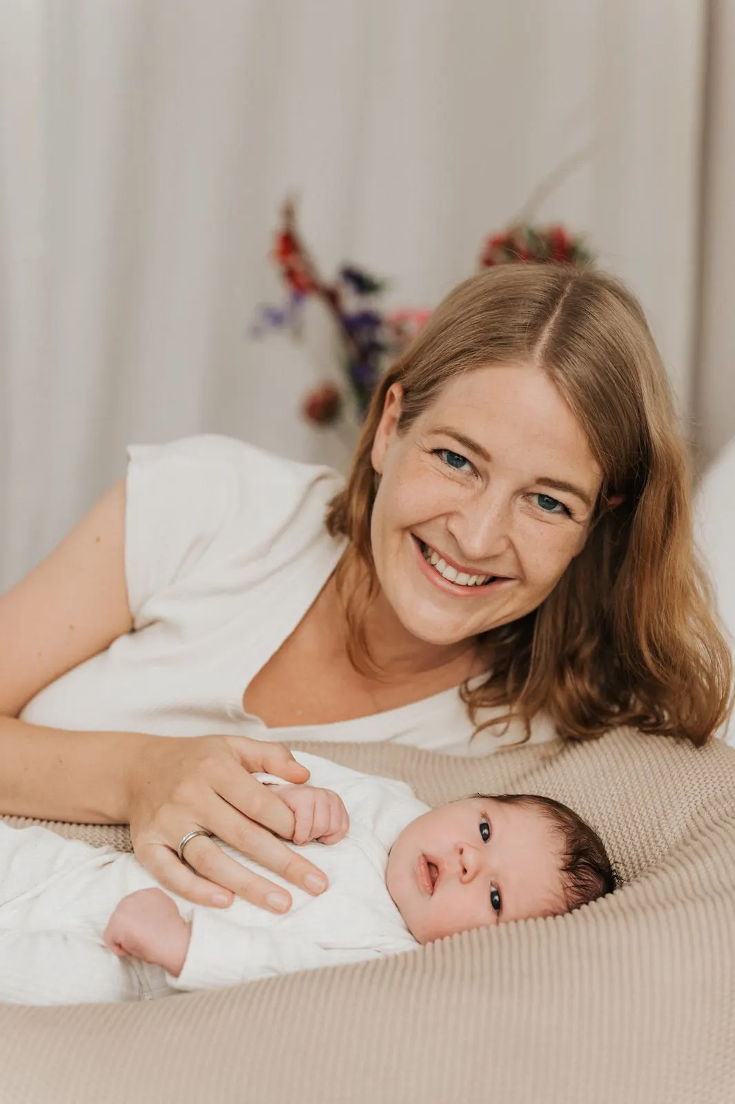 Mutter liegt lächelnd neben ihrem Neugeborenen auf dem Stillkissen, Babyfotografie Julia Aßmann