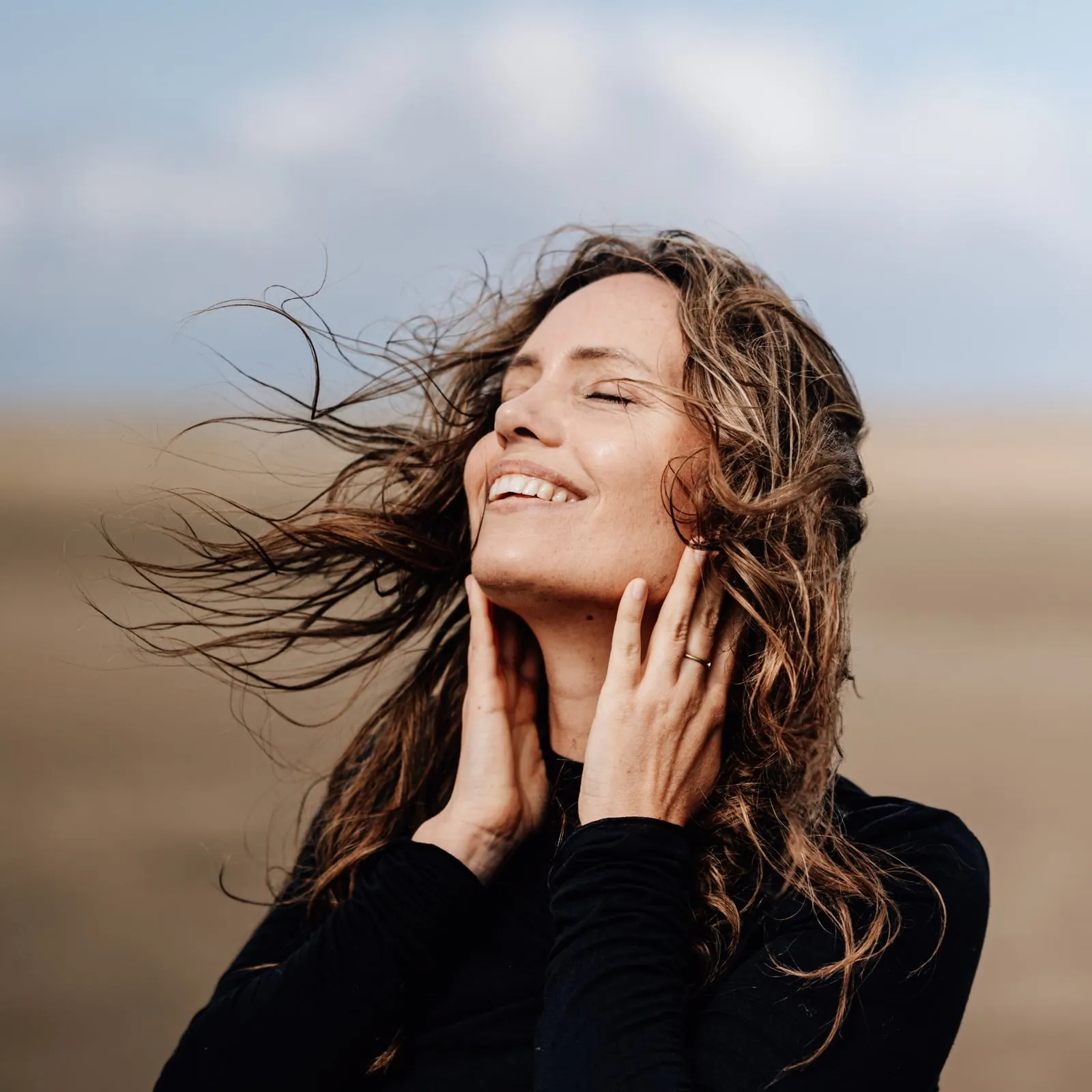 Frau lacht mit geschlossenen Augen im Wind am Strand, Portraitfotografie Julia Aßmann